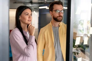 Two professionals brainstorming customer support strategies in front of a glass wall with sticky notes.